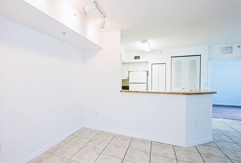 an empty living room with a kitchen and a tiled floor