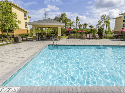 A pool with a gazebo and chairs around it. at Heron Pond 55+ Apartments, Florida