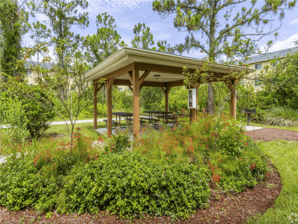 A wooden gazebo is surrounded by green plants and trees.