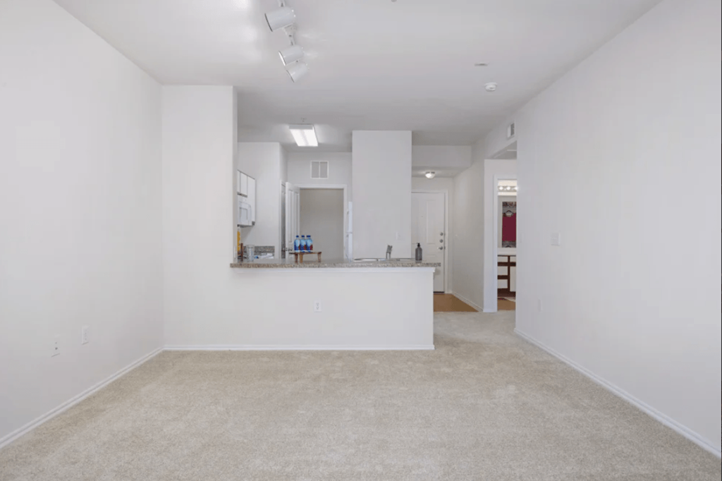 a living room and kitchen with white walls and carpet at Belle at Bay Colony 55+ Apartments, Texas