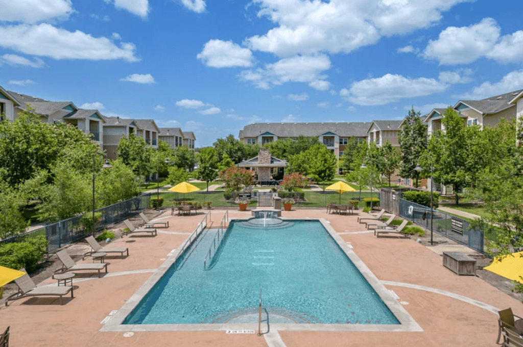 a pool with lounge chairs and umbrellas at the resort on a sunny day at Belle at Bay Colony 55+ Apartments, Dickinson, 77539