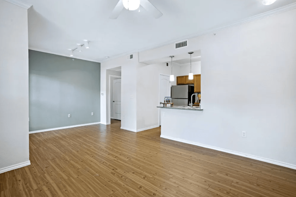 an empty living room and kitchen with wood floors and white walls at Ten 06 at Joshua Station Apartments, Texas