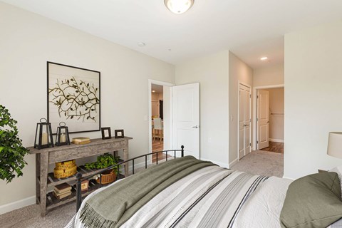 A bedroom with a bed, a table with a plant, and a painting on the wall. at Avery Landing Apartments, Greenville, 29605