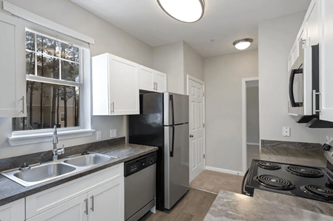 A kitchen with a black refrigerator and a window with a view of trees.