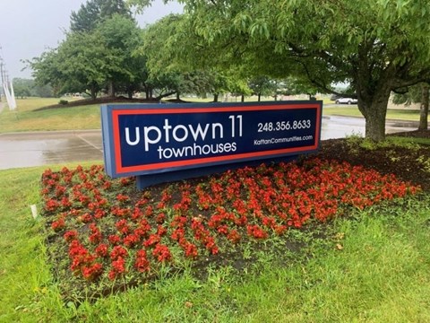 a sign for uptown 11 townhouses in a bed of red flowers