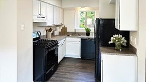 A black refrigerator sits in a kitchen with white cabinets.