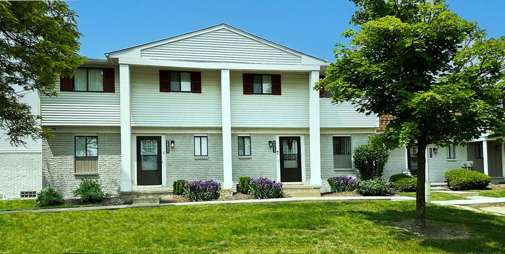 A white house with a grey roof and a green lawn in front.