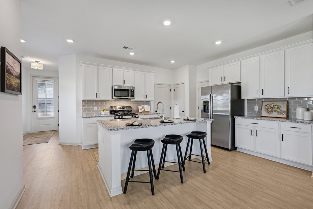 A kitchen with white cabinets and a white island with three black stools.