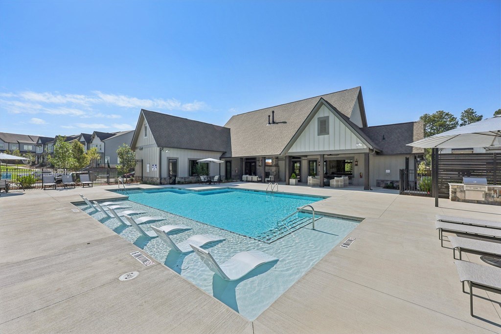 A large outdoor swimming pool with lounge chairs and a building in the background.