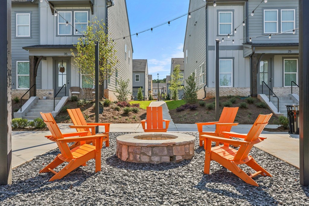 A small fire pit surrounded by orange chairs in front of apartment buildings.