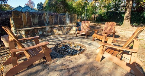 A fire pit surrounded by wooden chairs in a backyard setting.