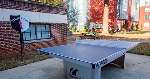 A ping pong table is set up outside a building with a sign that says "your turn".