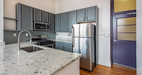 A kitchen with a granite counter top and a stainless steel refrigerator.