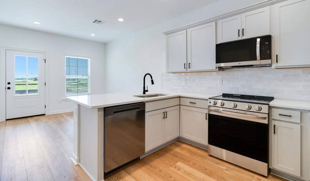 A kitchen with white cabinets and a black microwave.