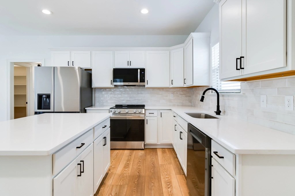 A modern kitchen with white cabinets and a wooden floor.