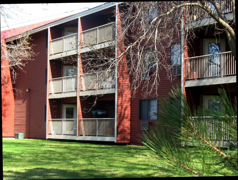 a red apartment building with balconies and green grass