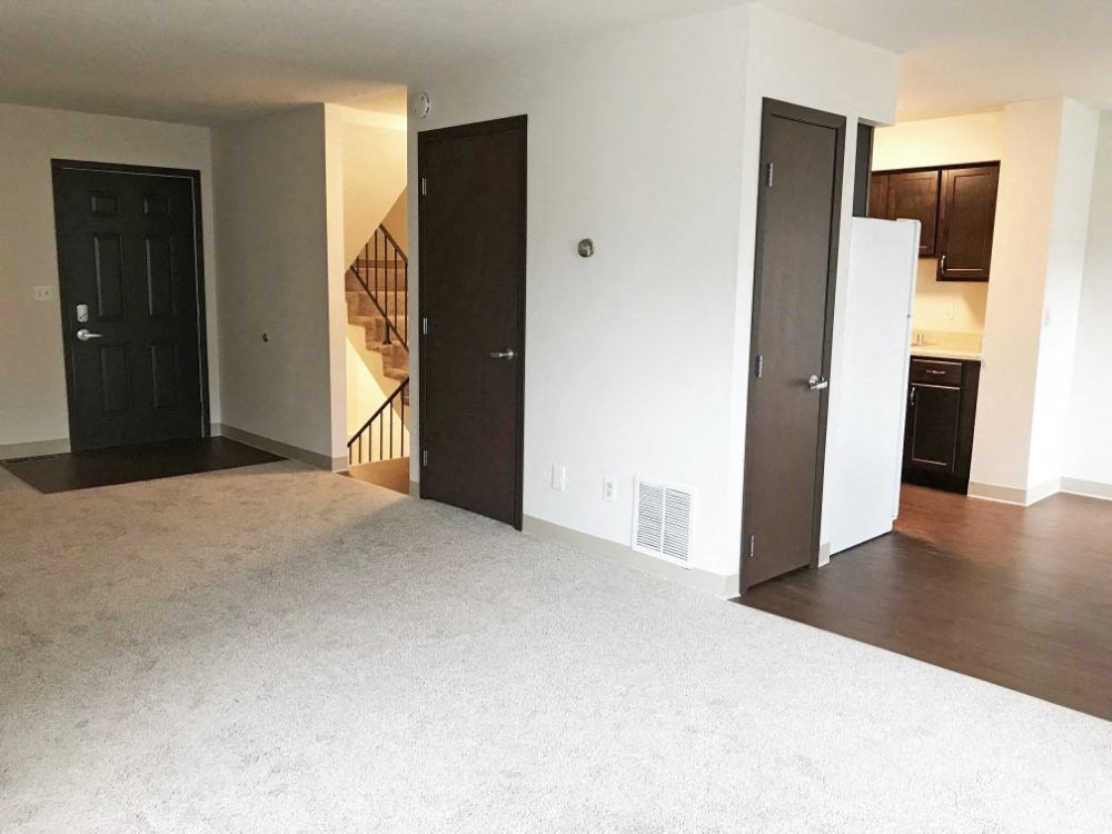 an empty living room with a refrigerator and a door to a kitchen
