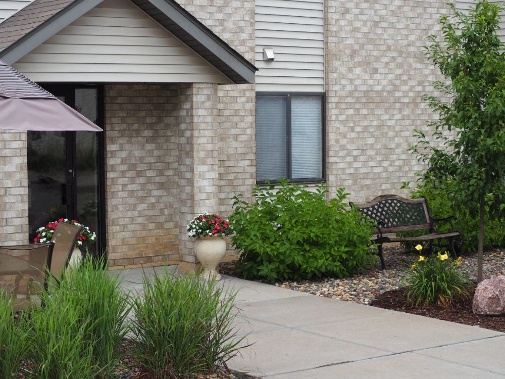 a sidewalk in front of a house with plants and a bench