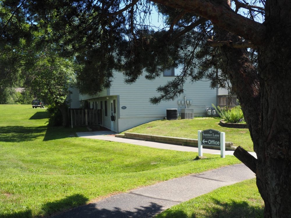 the front of a white house with a sidewalk and a sign