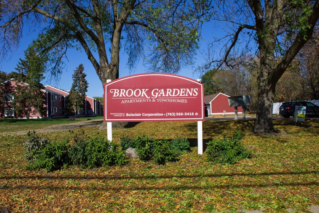 a sign for brook gardens in front of a red barn
