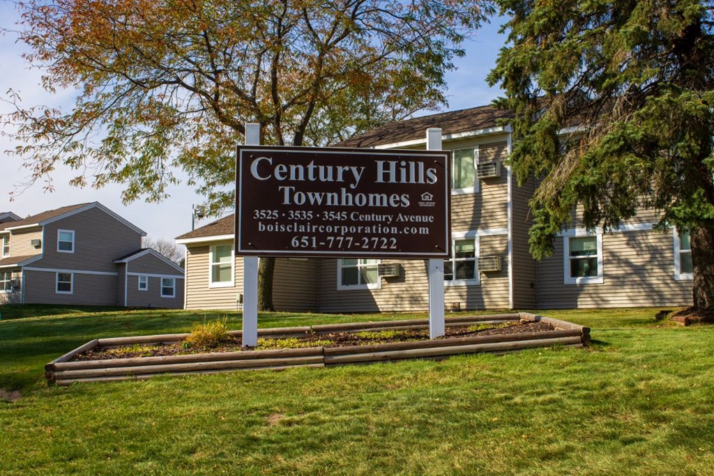 a sign for the century hills townhomes in front of a grassy field