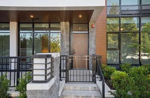 A modern house entrance with a wooden door and a black railing.