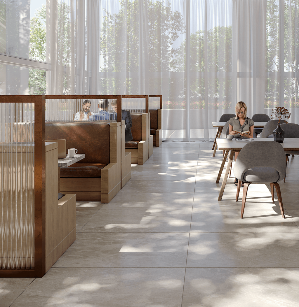 A woman is sitting at a table in a brightly lit room with large windows.