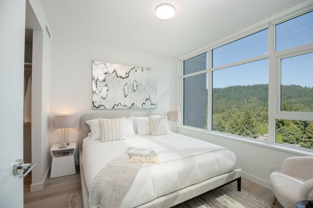 A bedroom with a large bed and a view of the forest outside the window.