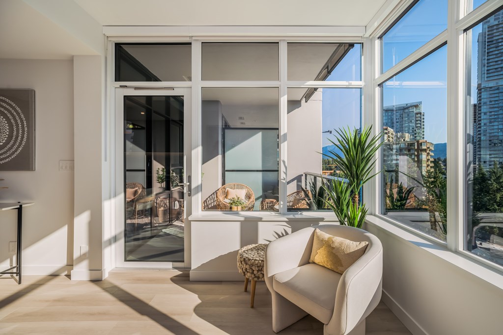 A white chair with a yellow pillow is in the foreground of a room with a view of the city.