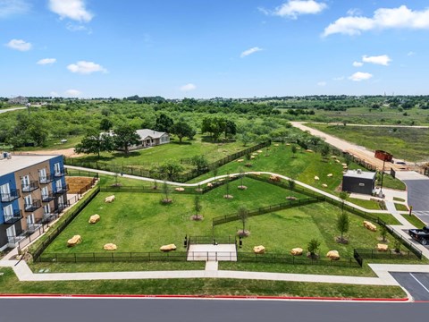 A large grassy area with trees and a fence in the foreground and a building to the left.