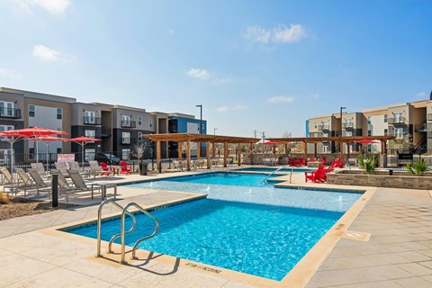 A swimming pool surrounded by red chairs and umbrellas.