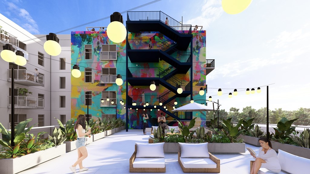 A woman is sitting on a white couch on a balcony with a colorful building in the background.