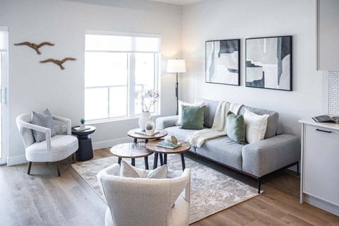 A living room with a grey couch, a white chair, and a table with a vase on it.