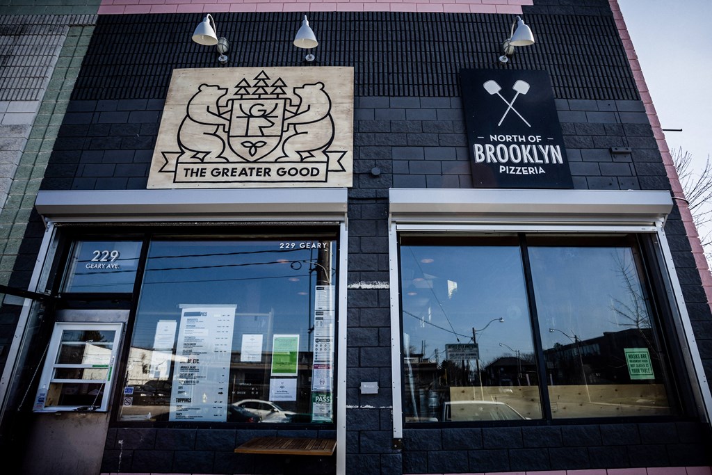 The front of a pizzeria with a black and white sign that says