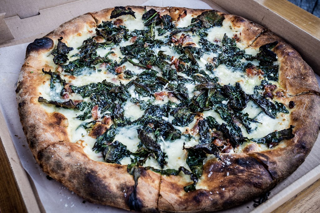 A pizza with spinach and cheese in a box.