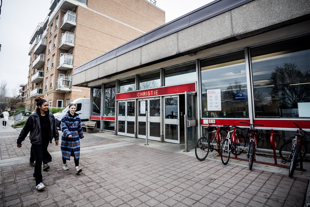 Two people walking in front of a building with a red sign that says