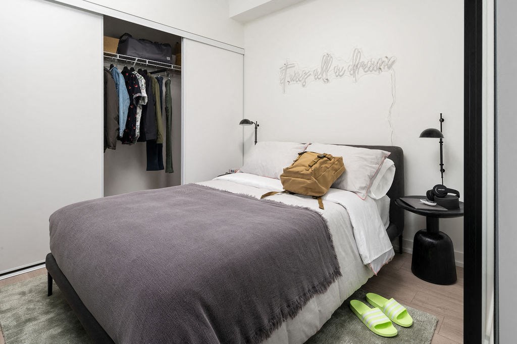 A bedroom with a bed, a nightstand, and a closet with clothes.