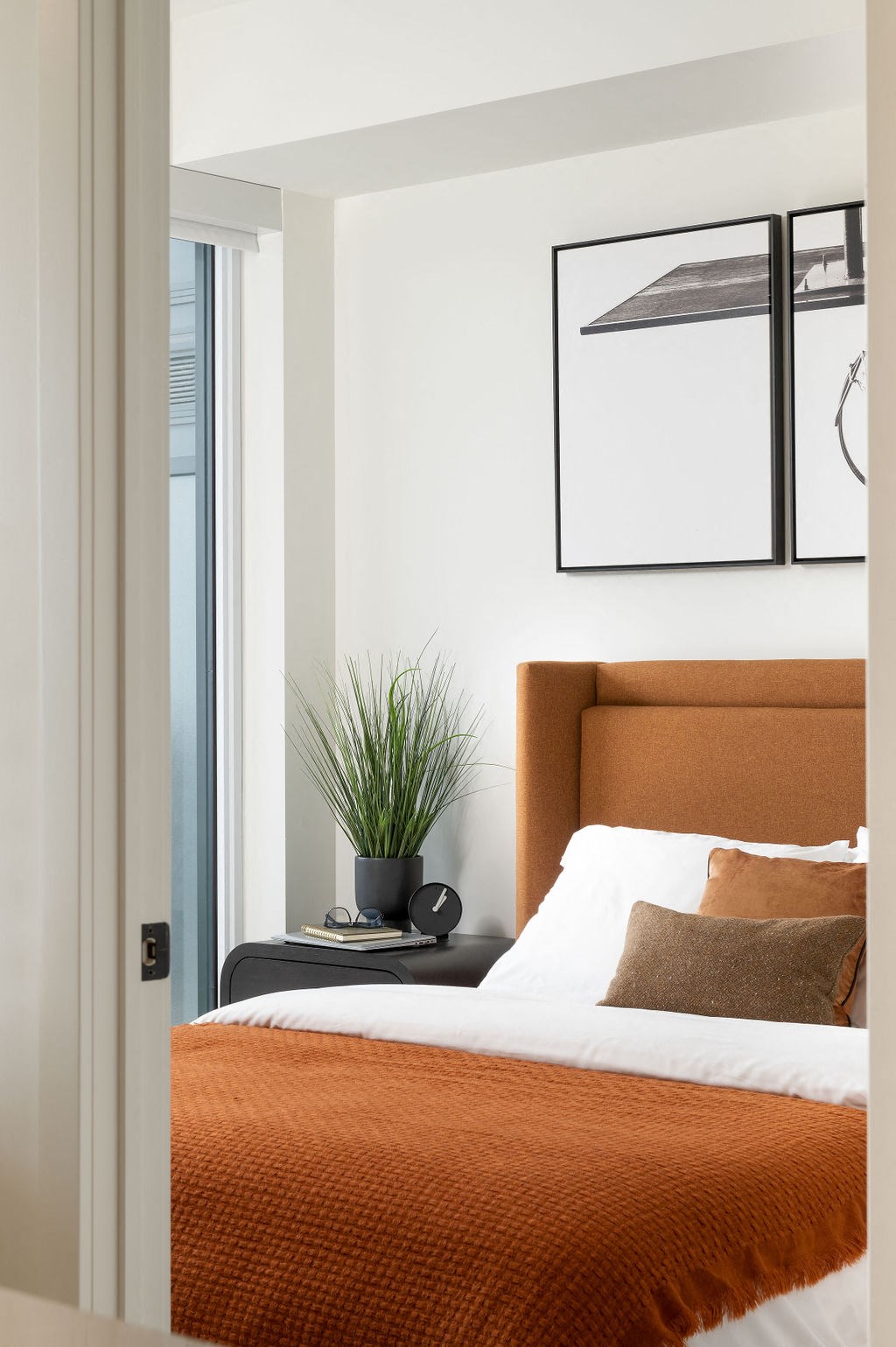 A bedroom with a bed, pillows, a potted plant, and a picture on the wall.