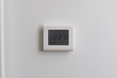 A white thermostat on a white wall.