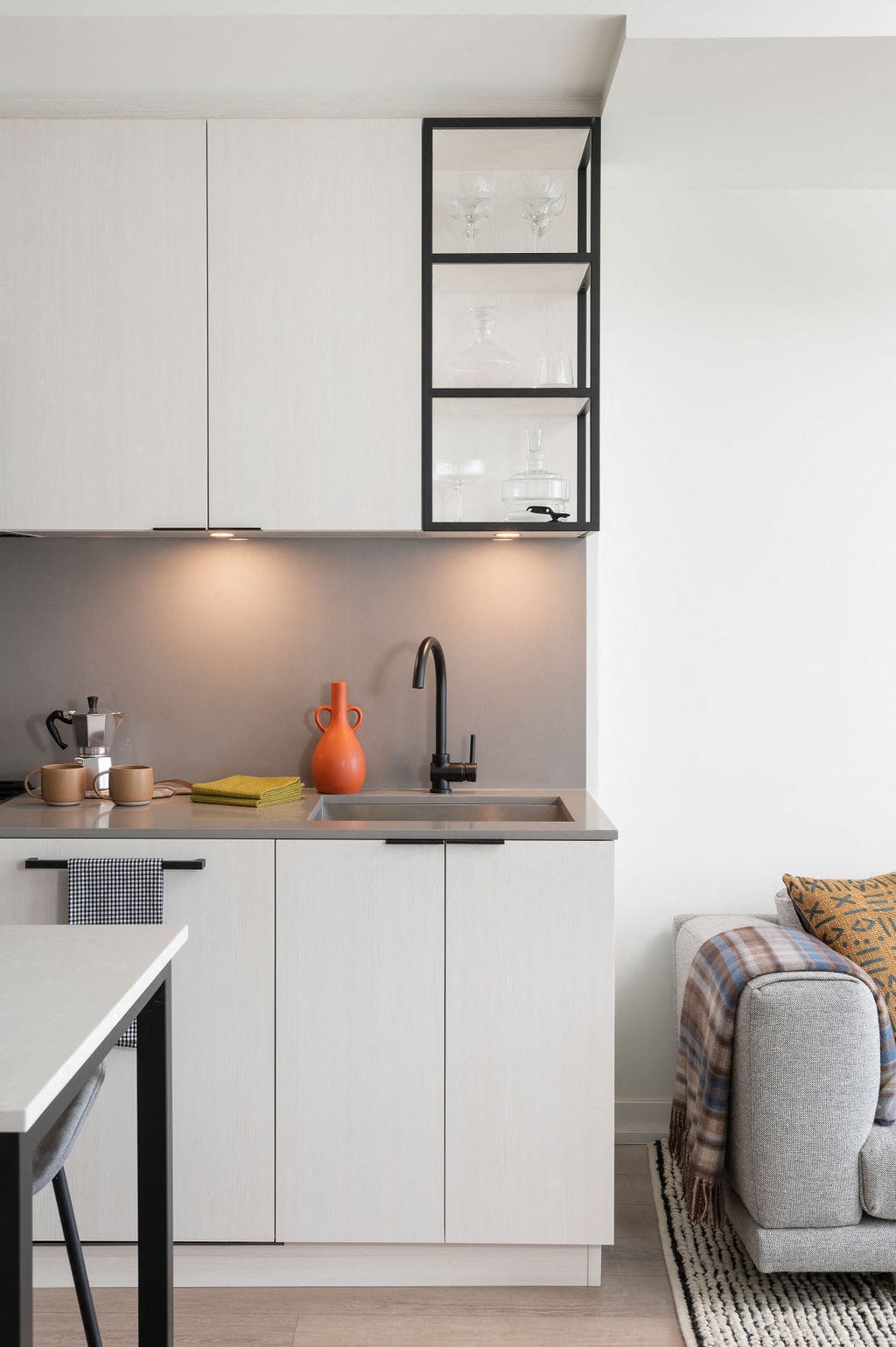 A kitchen with white cabinets and a grey chair.