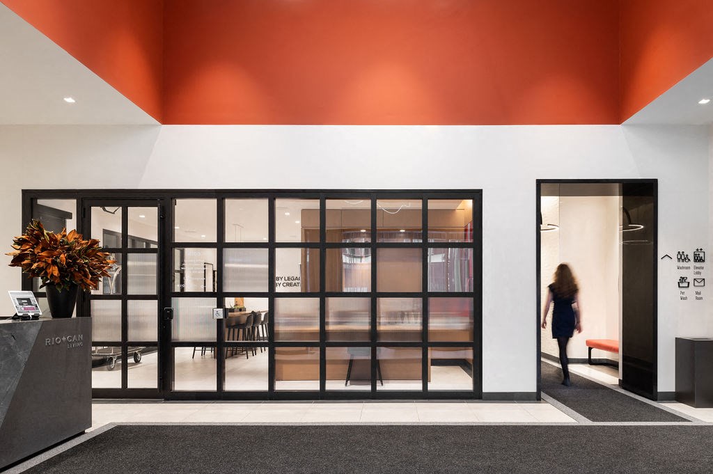 A woman walks into a brightly lit hallway with a black reception desk.