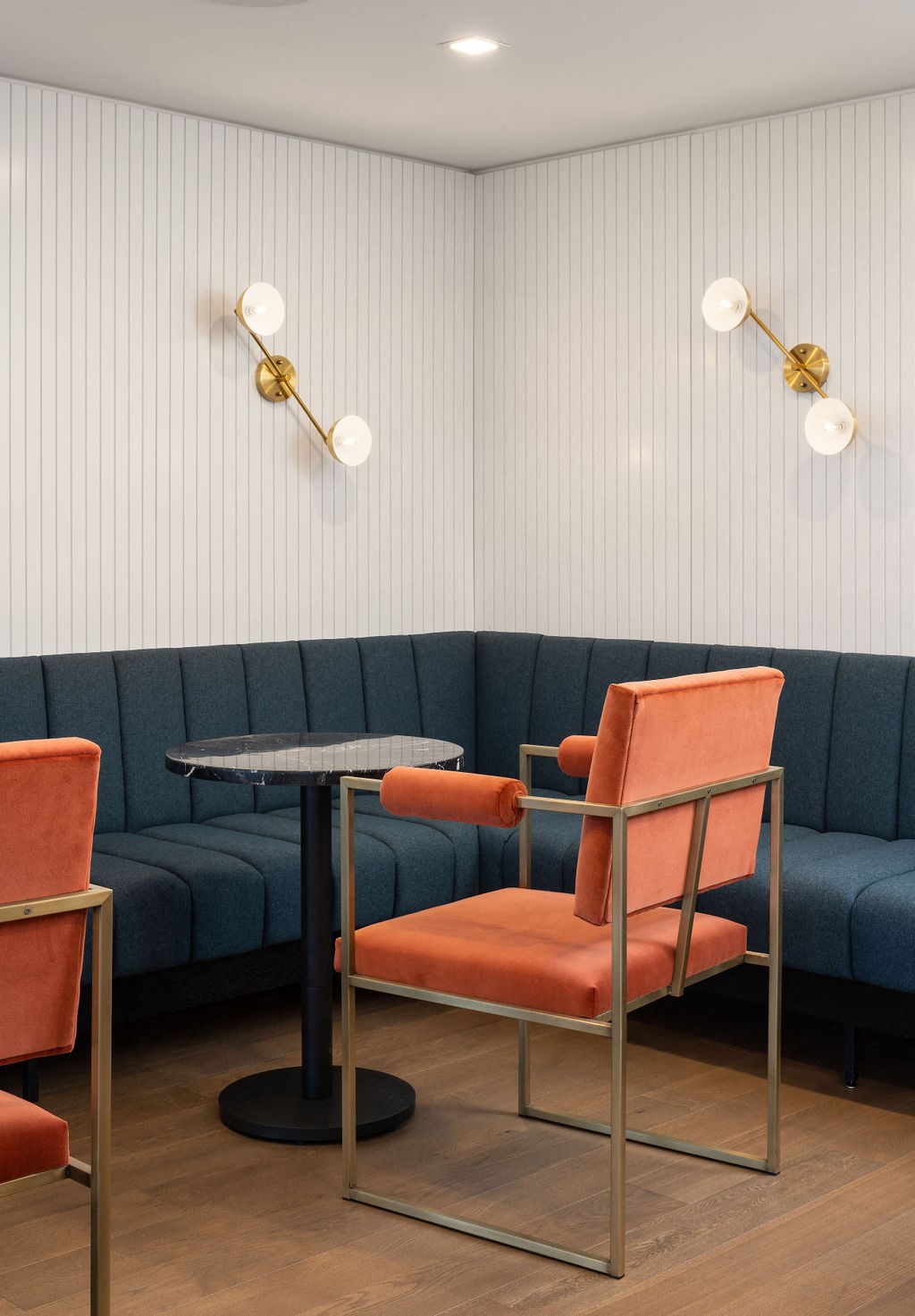 A blue couch with a black table and two chairs with orange cushions.