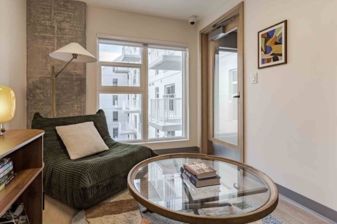 A living room with a green couch, a glass table, and a lamp.