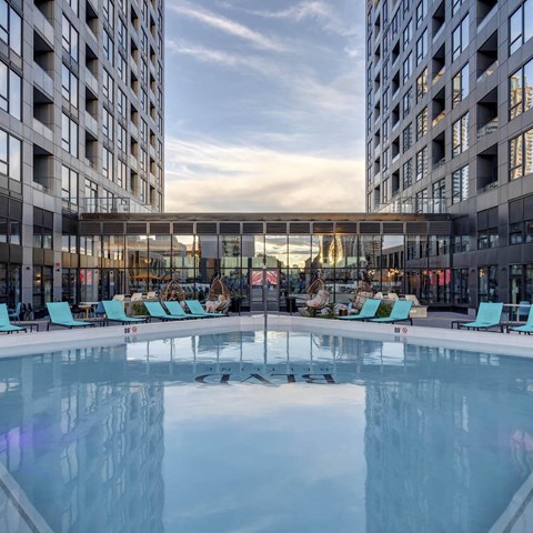 A large indoor swimming pool with lounge chairs is surrounded by two tall buildings.
