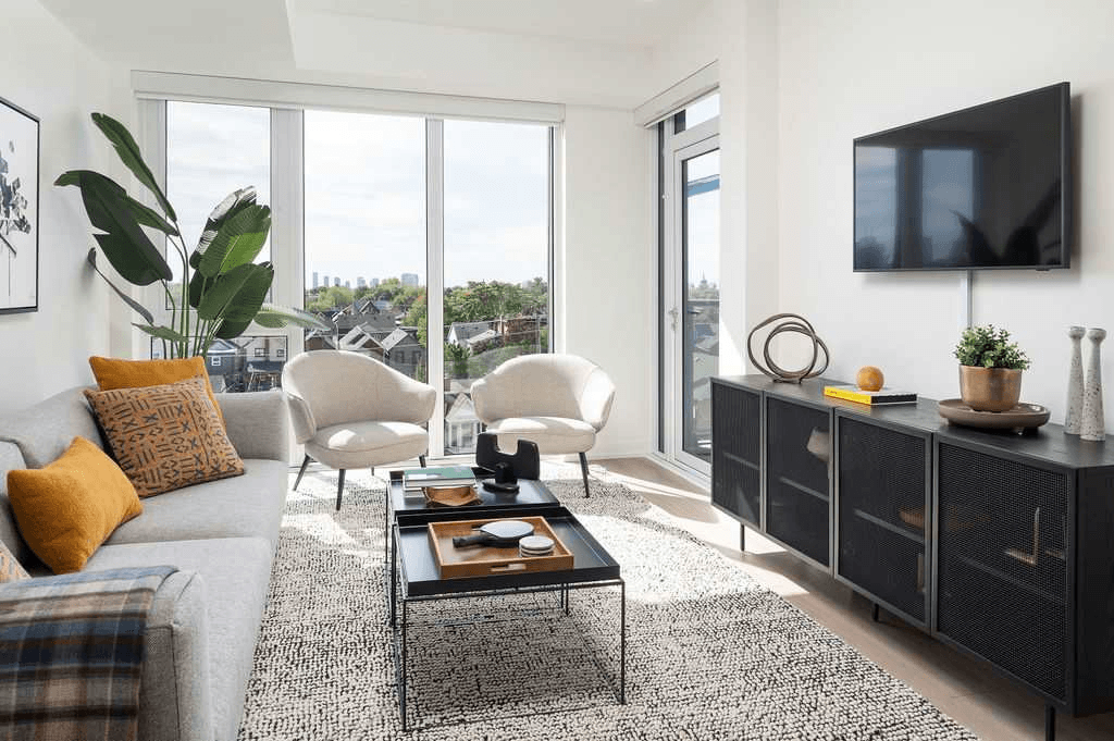 A living room with a grey couch, a coffee table, and a flat screen TV mounted on the wall.