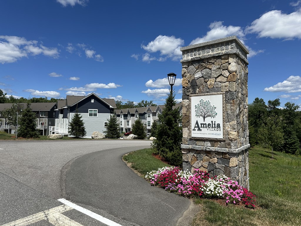 A stone pillar with a sign that says Amelia in front of a road.