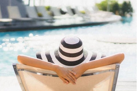 a woman with a hat sitting in a chair by a pool