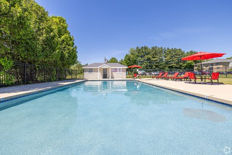 A swimming pool with red umbrellas and a building in the background.
