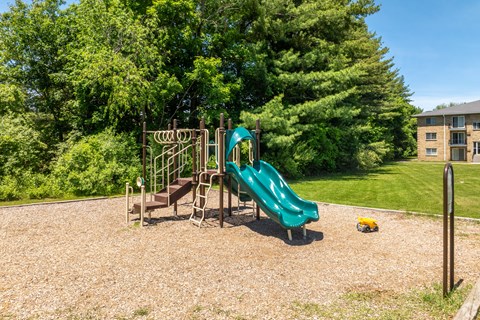 A playground with a green slide and a brown swing set.