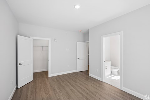 A room with a toilet in the corner and a door open to another room.